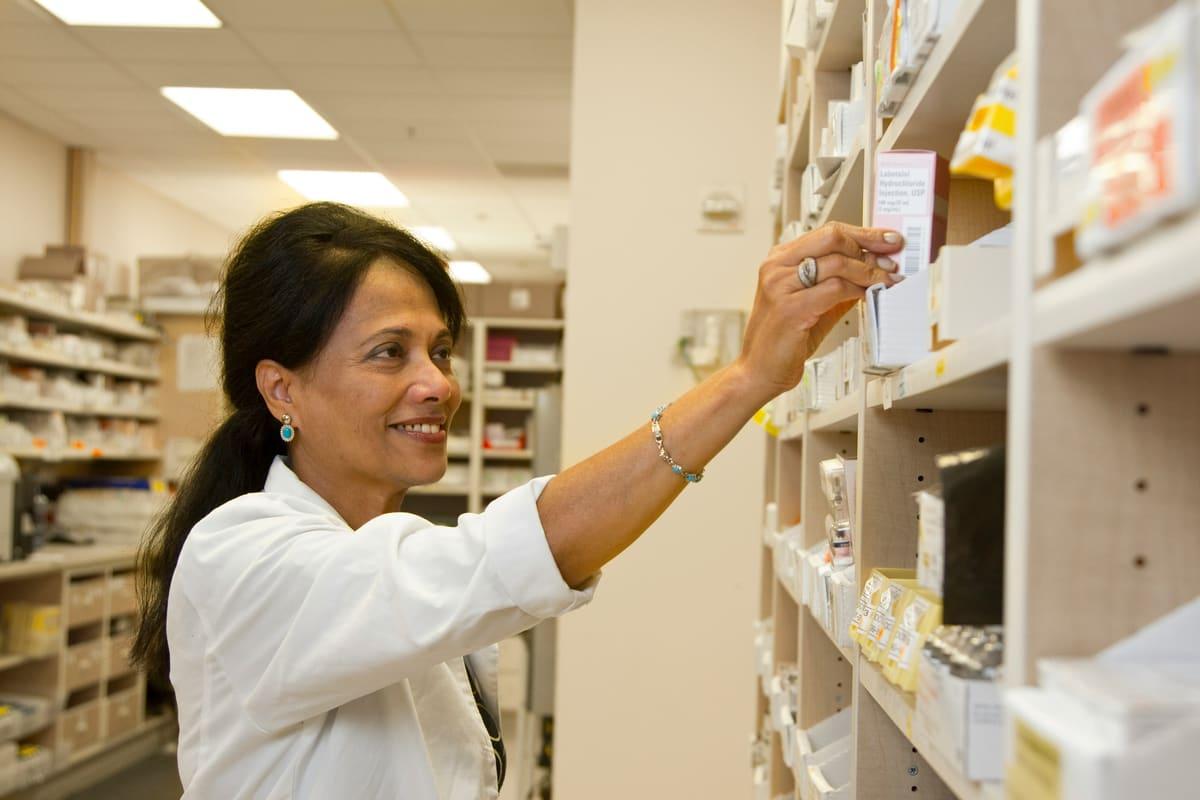 A pharmacist reaching for medication on a shelf